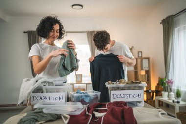 Anne ve oğul evlerinde durup bağış için kıyafet seçiyorlar. Genç, deli ve beyaz kadınlar evlerinin oturma odasındaki kutulara gardırop düzenliyorlar.