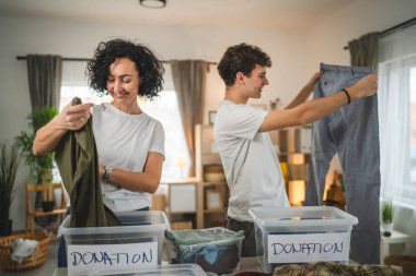 Anne ve oğul evlerinde durup bağış için kıyafet seçiyorlar. Genç, deli ve beyaz kadınlar evlerinin oturma odasındaki kutulara gardırop düzenliyorlar.