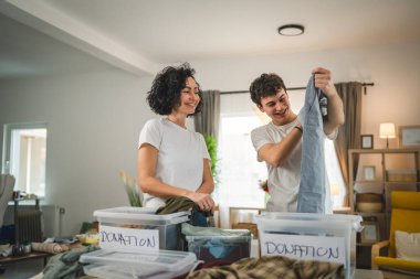Anne ve oğul evlerinde durup bağış için kıyafet seçiyorlar. Genç, deli ve beyaz kadınlar evlerinin oturma odasındaki kutulara gardırop düzenliyorlar.