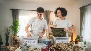 Anne ve oğul evlerinde durup bağış için kıyafet seçiyorlar. Genç, deli ve beyaz kadınlar evlerinin oturma odasındaki kutulara gardırop düzenliyorlar.