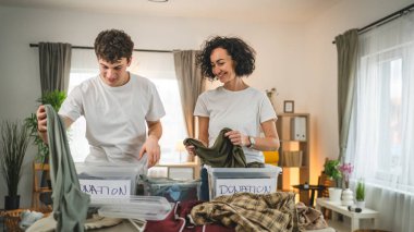 Anne ve oğul evlerinde durup bağış için kıyafet seçiyorlar. Genç, deli ve beyaz kadınlar evlerinin oturma odasındaki kutulara gardırop düzenliyorlar.