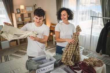 Anne ve oğul evlerinde durup bağış için kıyafet seçiyorlar. Genç, deli ve beyaz kadınlar evlerinin oturma odasındaki kutulara gardırop düzenliyorlar.