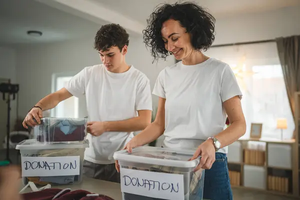 母亲和儿子站在家里 挑选衣服捐赠给疯了的少女和正在整理衣橱的高加索女人 放在他们公寓客厅的箱子里 — 图库照片
