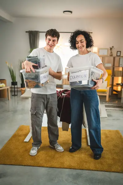 母亲和儿子站在家里 挑选衣服捐赠给疯了的少女和正在整理衣橱的高加索女人 放在他们公寓客厅的箱子里 — 图库照片