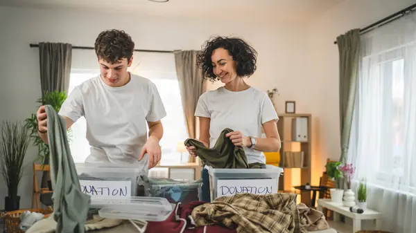 Anne ve oğul evlerinde durup bağış için kıyafet seçiyorlar. Genç, deli ve beyaz kadınlar evlerinin oturma odasındaki kutulara gardırop düzenliyorlar.