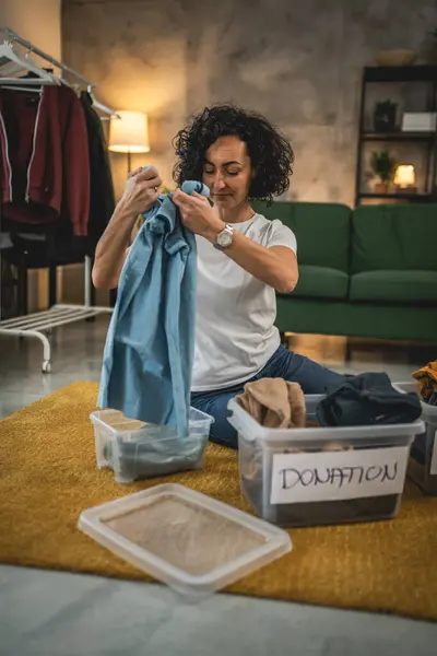 Yetişkin Kafkasyalı kadın evde, bağış için kıyafet dolabını düzenliyor.
