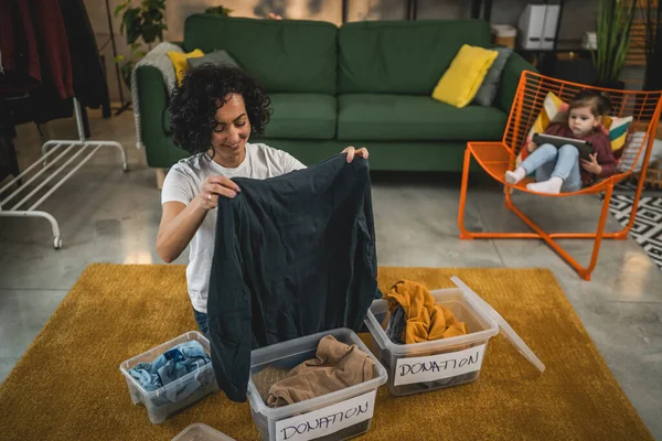Yetişkin Kafkasyalı kadın evde, bağış için kıyafet dolabını düzenliyor.