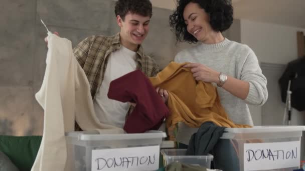 母亲和儿子站在家里 挑选衣服捐赠给疯了的少女和正在整理衣橱的高加索女人 放在他们公寓客厅的箱子里 — 图库视频影像