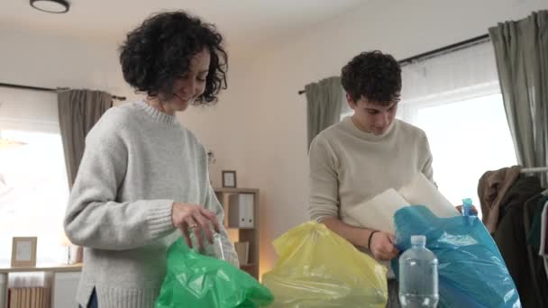 母親と息子の女性と10代の男の家族は 持続可能な生活のコンセプトを袋に廃プラスチック紙とガラスを分類する家庭でリサイクルします — ストック動画