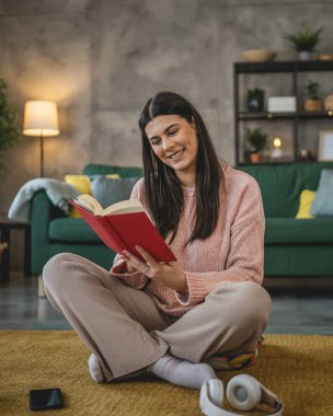 Genç bir yetişkin kadın. Bir kadın evde kitap okuyor ya da okuyor.