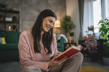 Genç bir yetişkin kadın. Bir kadın evde kitap okuyor ya da okuyor.