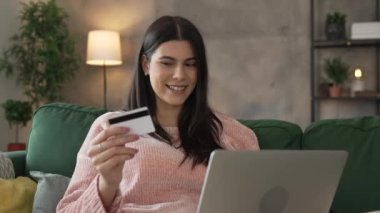 Genç bir yetişkin kadın evde oturup kredi kartı alışverişini internetten yapıyor.