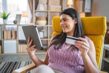 Genç bir yetişkin kadın evde oturup kredi kartı alışverişini internetten yapıyor.