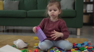 Beyaz tenli bir kız evdeki yerde tuğla bloklarla oynuyor.