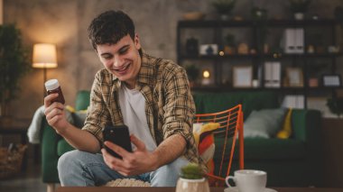 Bir adam ilaç tutuyor. İlaç şişesi hapları. Cep telefonunda etiketi yazıyor.