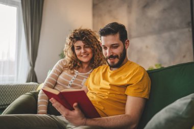 Erkek ve kadın Kafkasyalı yetişkin çift evde kanepe yatağında kitap okuyor.