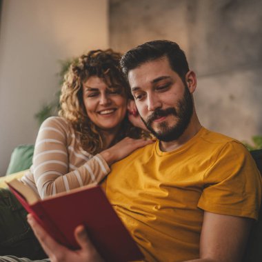 Erkek ve kadın Kafkasyalı yetişkin çift evde kanepe yatağında kitap okuyor.
