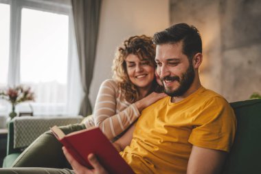 Erkek ve kadın Kafkasyalı yetişkin çift evde kanepe yatağında kitap okuyor.