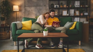 Erkek ve kadın Kafkasyalı yetişkin çift evde kanepe yatağında kitap okuyor.