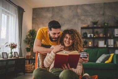Erkek ve kadın Kafkasyalı yetişkin çift evde kitap okuyor.