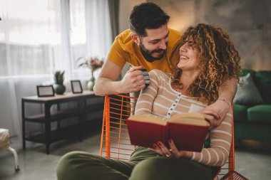 Erkek ve kadın Kafkasyalı yetişkin çift evde kitap okuyor.