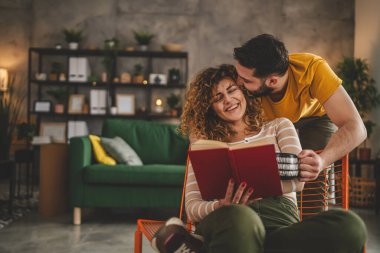 Erkek ve kadın Kafkasyalı yetişkin çift evde kitap okuyor.