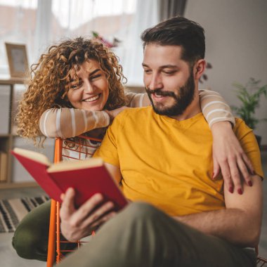 Erkek ve kadın Kafkasyalı yetişkin çift evde kitap okuyor.