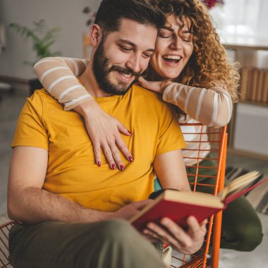 Erkek ve kadın Kafkasyalı yetişkin çift evde kitap okuyor.