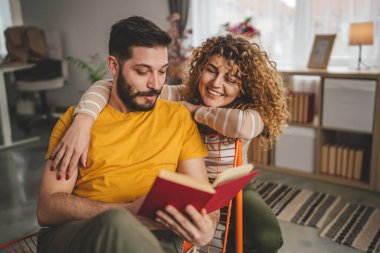 Erkek ve kadın Kafkasyalı yetişkin çift evde kitap okuyor.