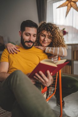 Erkek ve kadın Kafkasyalı yetişkin çift evde kitap okuyor.