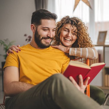 Erkek ve kadın Kafkasyalı yetişkin çift evde kitap okuyor.