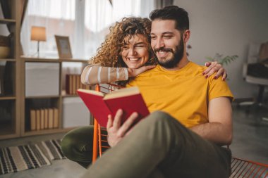 Erkek ve kadın Kafkasyalı yetişkin çift evde kitap okuyor.