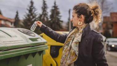 Bir yetişkin kadın cam atık ve yeşil poşetlerle geri dönüşüm kaplarının önünde duruyor ve sıfır atık eko kavramını yeniden kullanmak için şişe kavanozu fırlatıyor.