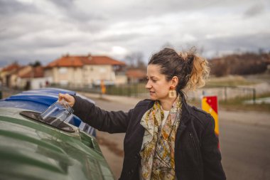 Bir yetişkin kadın cam atık ve yeşil poşetlerle geri dönüşüm kaplarının önünde duruyor ve sıfır atık eko kavramını yeniden kullanmak için şişe kavanozu fırlatıyor.