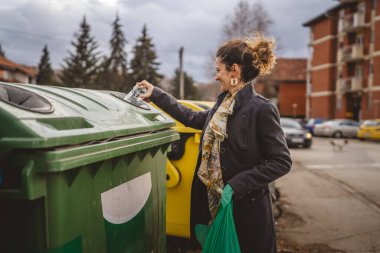 Bir yetişkin kadın cam atık ve yeşil poşetlerle geri dönüşüm kaplarının önünde duruyor ve sıfır atık eko kavramını yeniden kullanmak için şişe kavanozu fırlatıyor.