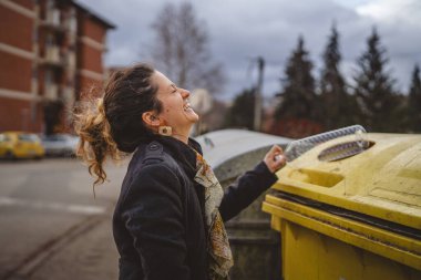 Bir yetişkin kadın, plastik atık ve sarı poşetlerle geri dönüşüm kutularının önünde duruyor ve sıfır atık eko kavramını yeniden kullanmak için şişe fırlatıyor.