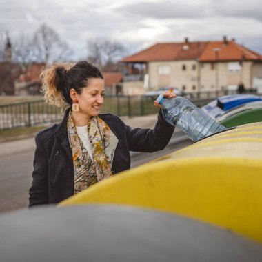 Bir yetişkin kadın, plastik atık ve sarı poşetlerle geri dönüşüm kutularının önünde duruyor ve sıfır atık eko kavramını yeniden kullanmak için şişe fırlatıyor.