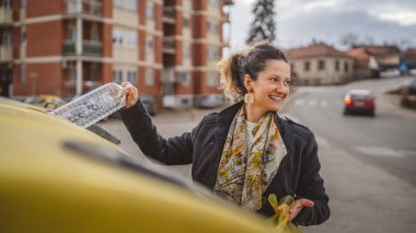 Bir yetişkin kadın, plastik atık ve sarı poşetlerle geri dönüşüm kutularının önünde duruyor ve sıfır atık eko kavramını yeniden kullanmak için şişe fırlatıyor.