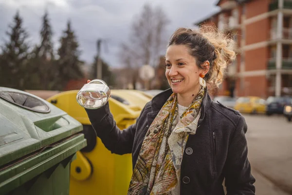 Bir yetişkin kadın cam atık ve yeşil poşetlerle geri dönüşüm kaplarının önünde duruyor ve sıfır atık eko kavramını yeniden kullanmak için şişe kavanozu fırlatıyor.