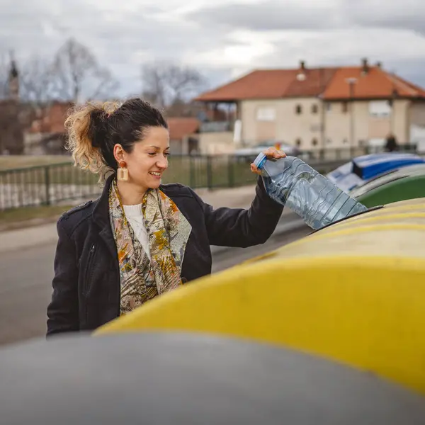 Bir yetişkin kadın, plastik atık ve sarı poşetlerle geri dönüşüm kutularının önünde duruyor ve sıfır atık eko kavramını yeniden kullanmak için şişe fırlatıyor.