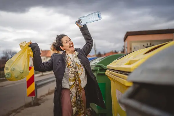 Bir yetişkin kadın, plastik atık ve sarı poşetlerle geri dönüşüm kutularının önünde duruyor ve sıfır atık eko kavramını yeniden kullanmak için şişe fırlatıyor.