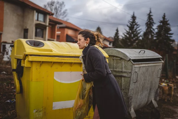 Bir yetişkin kadın, plastik atık ve sarı poşetlerle geri dönüşüm kutularının önünde duruyor ve sıfır atık eko kavramını yeniden kullanmak için şişe fırlatıyor.