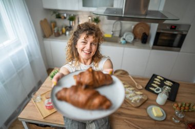 Yetişkin bir Kafkasyalı kadın her sabah kahvaltıda taze kruvasanla mutfakta duruyor.