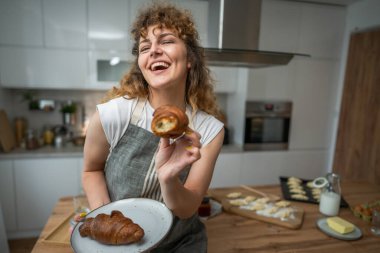 Yetişkin bir Kafkasyalı kadın her sabah kahvaltıda taze kruvasanla mutfakta duruyor.