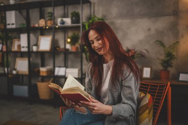 Genç bir yetişkin kadın. Bir kız öğrenci kitap okuyor ya da evde çalışıyor. Kızıl saç fotokopi alanı.