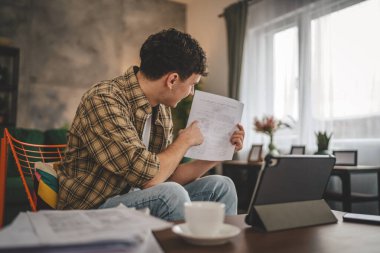 Kafkasyalı genç adam evde oturur dijital tablet kullanır. Belge ya da burs belgesi gösterir. Sınav sonuçları evde mutlu bir gülüş videosu çeker.