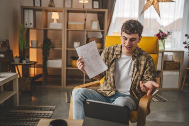Kafkasyalı genç adam evde oturur dijital tablet kullanır. Belge ya da burs belgesi gösterir. Sınav sonuçları evde mutlu bir gülüş videosu çeker.