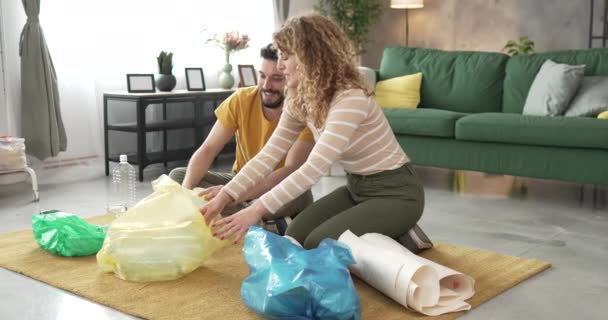 夫妻男女家庭在家里回收利用废纸和废玻璃到绿色 黄色和蓝色袋子的可持续生活理念 — 图库视频影像