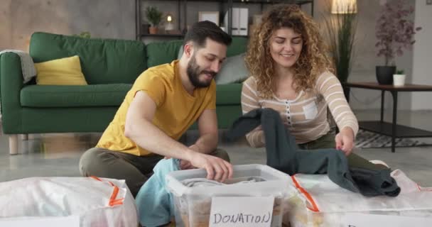 丈夫和妻子夫妇在家里挑选衣服捐赠 将衣橱分类到他们公寓客厅的箱子里 — 图库视频影像