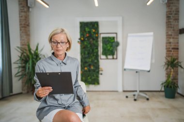 Ofiste kendine güvenen bir fotokopi odasında gözlüklü, olgun, beyaz bir kadının portresi.